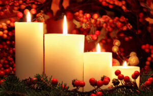 Photo of four lit candles with holly berries